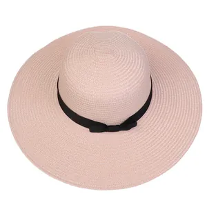 Close-up of light pink woven straw sun hat featuring a classic black ribbon bow detail