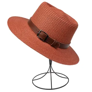 Detail of brick red woven straw sun hat with leather strap and silver metal buckle