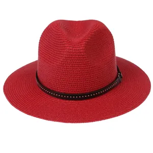 Detail of red straw Fedora hat featuring a brown leather band and silver metal studs