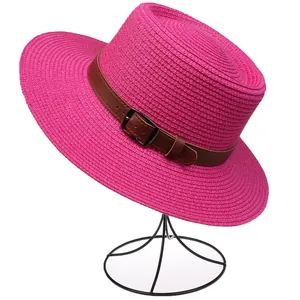 Detail of rose red woven straw hat featuring a brown leather strap and metal buckle