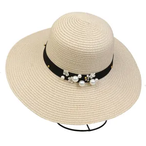 Detail of beige straw sun hat featuring elegant pearls, white petals, and black ribbon strap