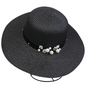 Close-up of black straw sun hat with decorative pearls, white flowers and golden rivets