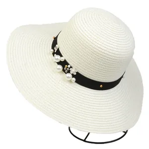 Detail of cream straw sun hat with black ribbon, pearls, and 3D floral accents