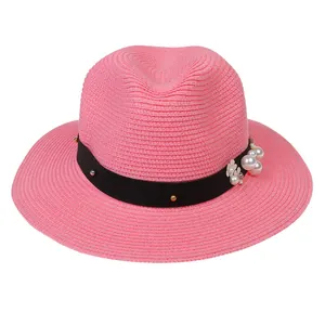 Détail macro du chapeau Panama rose avec perles décoratives, fleurs blanches et ruban clouté