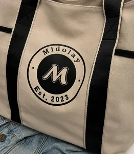 Primer plano de bolso tote de lona beige con correas negras y detalle de logotipo
