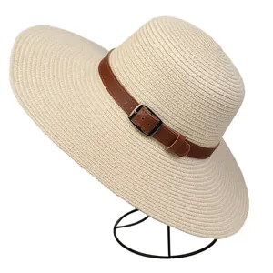 Detail of cream straw sun hat featuring a round top and brown leather band with metal buckle