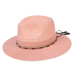 Detail of pink woven straw hat featuring golden chain trim and fringe tassels