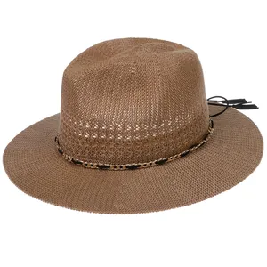 Detail of coffee brown woven straw hat featuring a gold chain band and black tassels