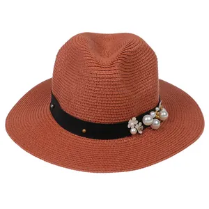 Détail d'un chapeau Panama rouge brique orné d'un ruban à fleurs blanches et de perles