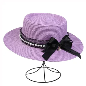 Detailed view of purple woven straw hat with black lace, pearls and a large side bow
