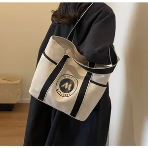 Bolso tote grande de lona con asas de rayas negras llevado por una modelo femenina