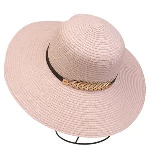 Detail of pink straw sun hat featuring a brown decorative band and golden feather ornament