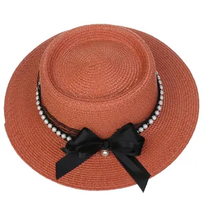 Detail of rust red straw hat featuring a black satin bow and white pearl accents