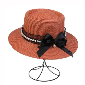Detail of red straw boater hat featuring black lace, pearls, and large bow decoration