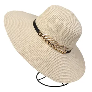 Close-up of woven straw sun hat with black leather band and golden metal leaf detail
