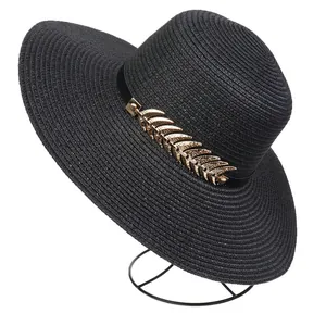 Detail of black wide brim straw hat with elegant ribbon and golden metal leaf charm
