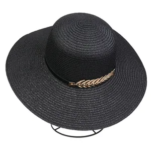 Detail of black straw beach hat featuring elegant gold leaf metal accessory and ribbon