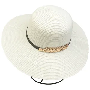 Detail of cream straw hat with thin black leather strap and golden leaf metal accessory