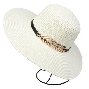 Detail of white woven sun hat featuring a delicate golden leaf buckle and black decorative band