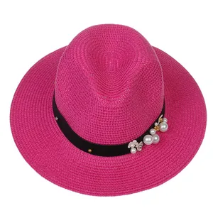 Détail d'un chapeau de paille rose fuchsia avec perles et broderie florale sur ruban noir