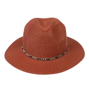 Detail of terracotta straw fedora featuring a golden metal chain and woven black ribbon