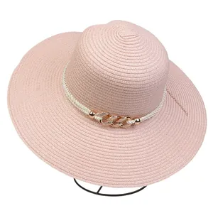 Detail of pink wide brim straw hat with white cord and gold chain accent on stand