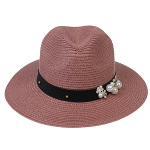 Détail d'un chapeau de soleil Panama rose avec ruban noir, perles et fleurs décoratives