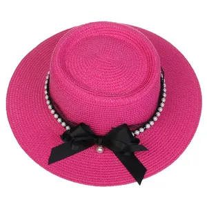 Detailed shot of bright pink straw boater hat with black bow, lace and pearl decoration