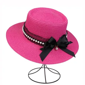 Detail of bright pink straw hat with black lace, faux pearls and a satin ribbon bow