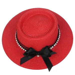 Detail of red boater straw hat featuring a black satin bow and white pearl chain trim