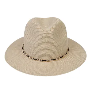 Detail of beige straw Panama hat featuring golden chain and black ribbon trim