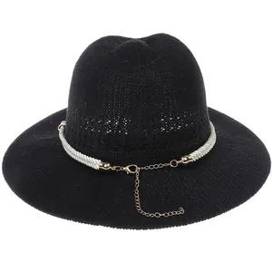 Detail of black woven straw hat featuring white cord trim and gold adjustable chain