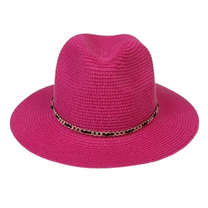 Detail of rose pink straw sun hat showing woven texture and gold chain with black ribbon