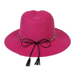 Detail of rose pink straw sun hat featuring elegant gold chains and black tassels