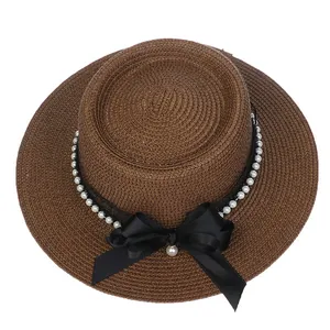 Detail of a brown straw boater hat featuring pearl accents and a black satin bow knot
