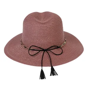 Detail of rose pink straw sun hat with gold chain, black bow, and tassel decoration