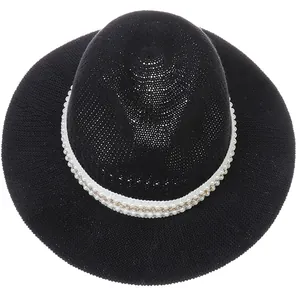 Detail of black woven fedora hat featuring white pearl ribbon and golden chain trim