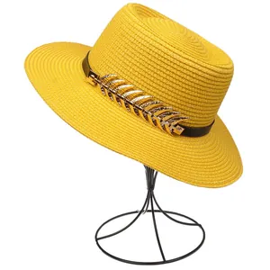 Detail of yellow straw sun hat featuring black band and golden metal leaf ornaments