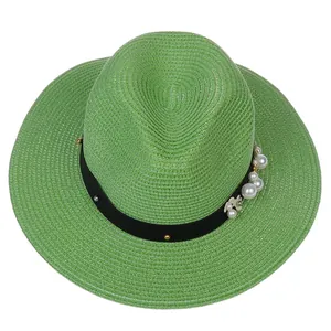 Détail d'un chapeau Panama vert avec texture tressée, ruban noir et accents de fleurs perlées