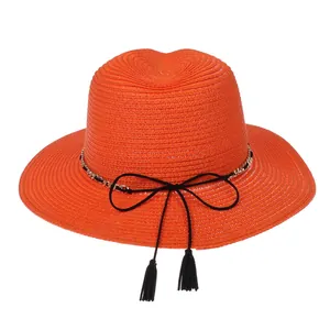 Detail of orange straw Panama hat with black ribbon bow, fringe, and gold chain accent