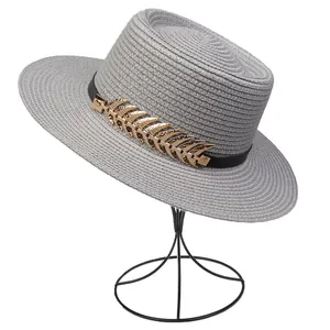 Detail of grey straw sun hat featuring black band and large golden leaf ornament