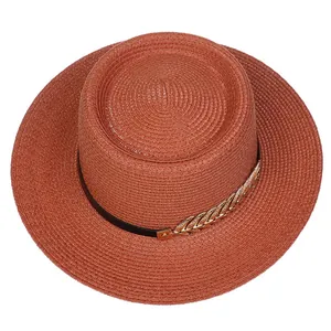 Close-up of terracotta straw hat with black ribbon and golden wheat metal buckle detail
