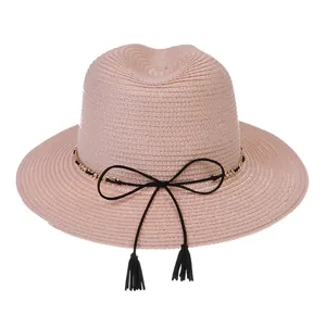 Detail of light pink straw Fedora featuring golden chain and tassel trim for summer