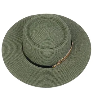 Detail of dark green straw hat with flat top, black band, and golden leaf ornament