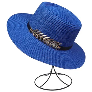 Detailed view of royal blue straw hat featuring black band and golden feather ornament