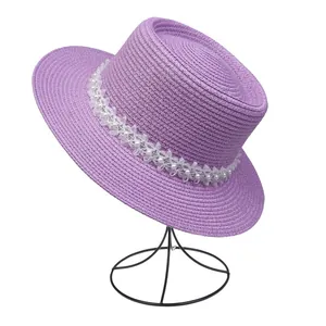 Detailansicht eines lila Strohhutes mit weißen Spitzenblumen und eleganten Perlen