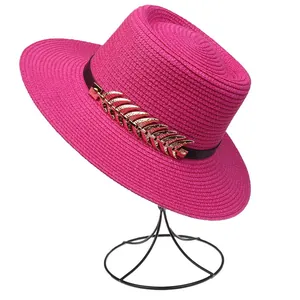 Detail of rose red straw hat with black leather band and golden feather buckle ornament