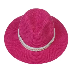 Détail du tissage d'un chapeau de paille rose fuchsia avec perles et chaîne dorée élégante