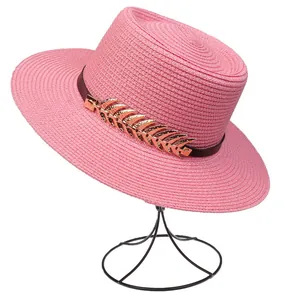 Close-up of pink straw hat featuring a brown leather band and a gold feather ornament