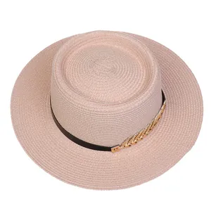Detail view of pink boater hat featuring fine straw texture and golden leaf ornament